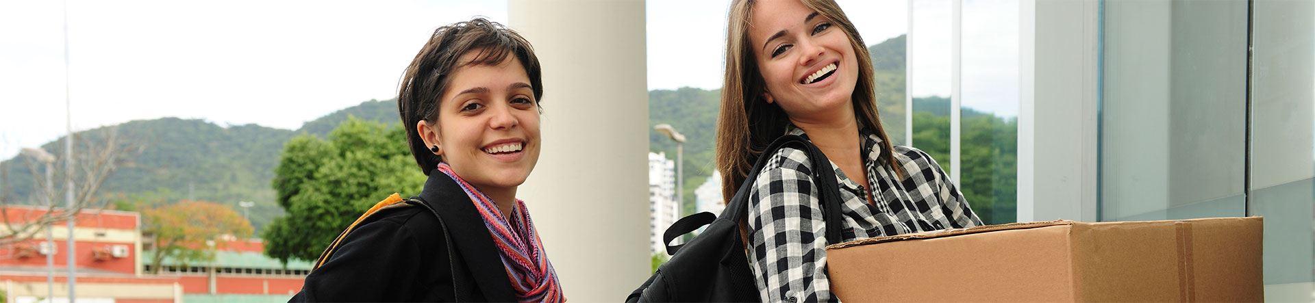 duas mulheres jovens brancas sorridentes com caixas e malas de mudança