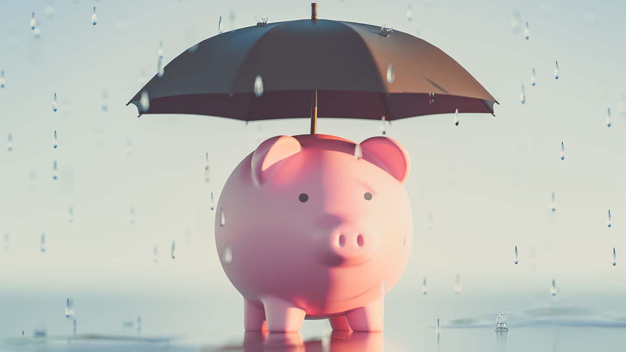 porquinho protegido por um guarda-chuva, representando a segurança da reserva de emergência